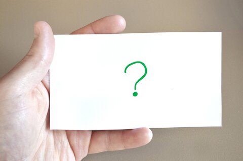 Ein Zettel mit einem günen Fragezeichen wird in der Hand gehalten.