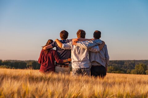 Anblick auf die Rücken von 4 Jugendlichen, die gemeinsam den Sonnenuntergang betrachten